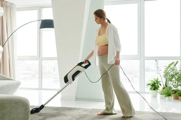 A pregnant woman in casual clothes vacuuming her living room's carpet